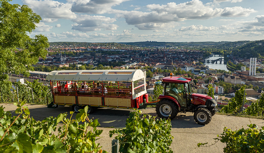 Planwagenfahrt in Würzburg mit rotem Traktor durch die Weinberge am Stein